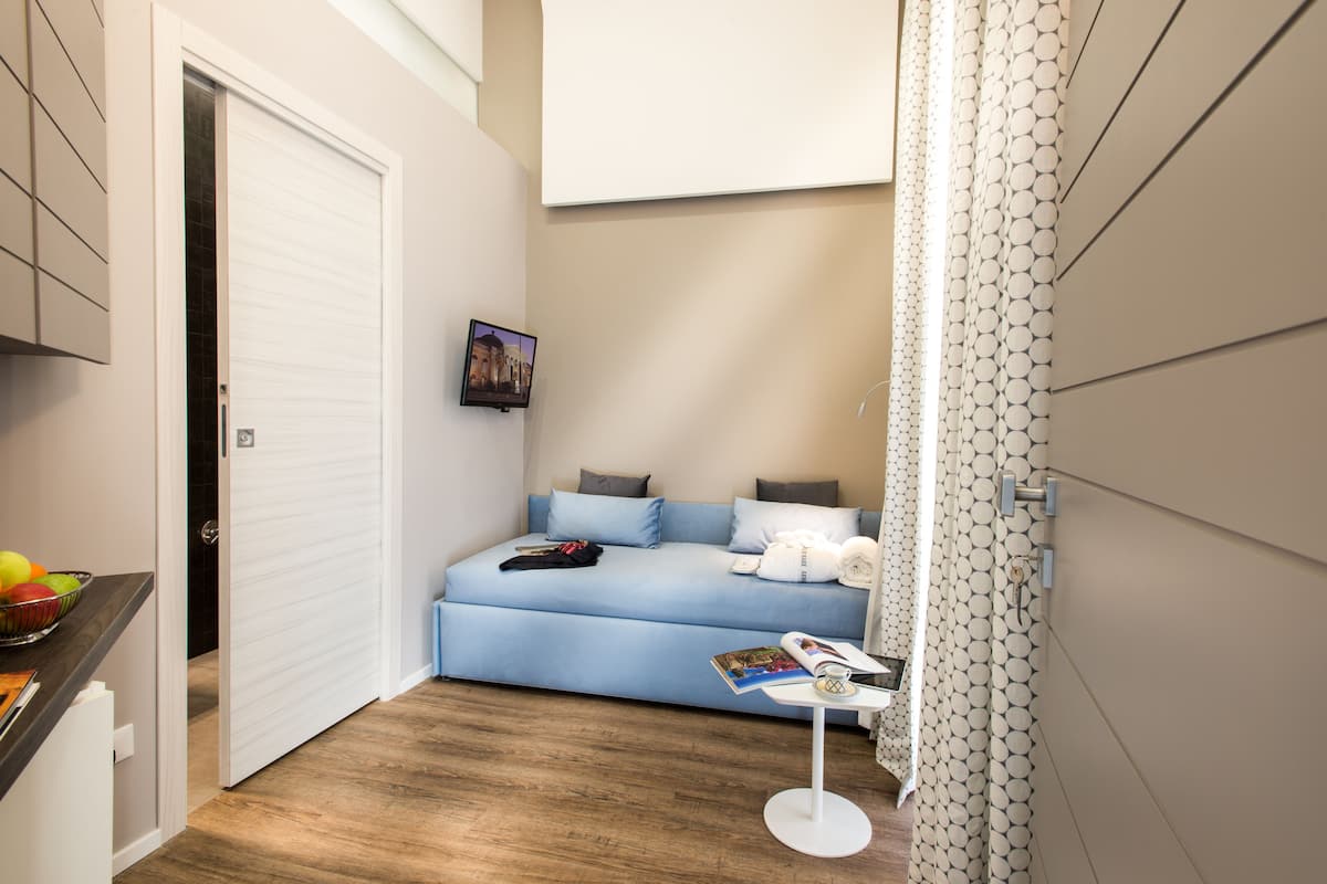 Un dormitorio pequeño con una cama individual, una mesita y un televisor instalado en la pared.
