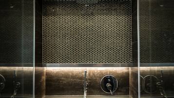 Cabina doccia moderna con pannello metallico forato e manopola di controllo.