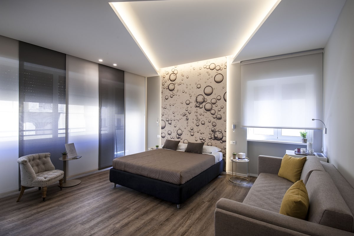 Un dormitorio moderno con una cama grande, un sofá, una silla, una mesita y una pared con diseños ondulados.