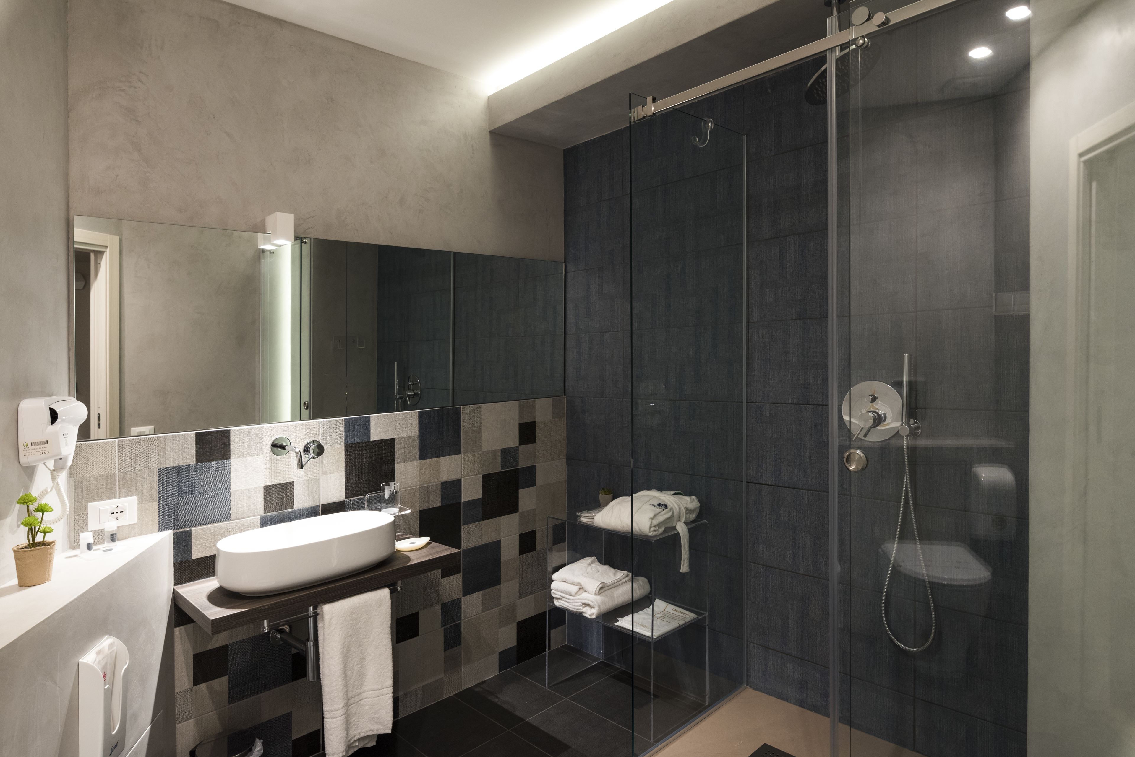 A modern bathroom with a large mirror, a white sink, a glass shower enclosure, and a towel rack.