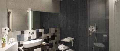 A modern bathroom with a large mirror, a white sink, a glass shower enclosure, and a towel rack.
