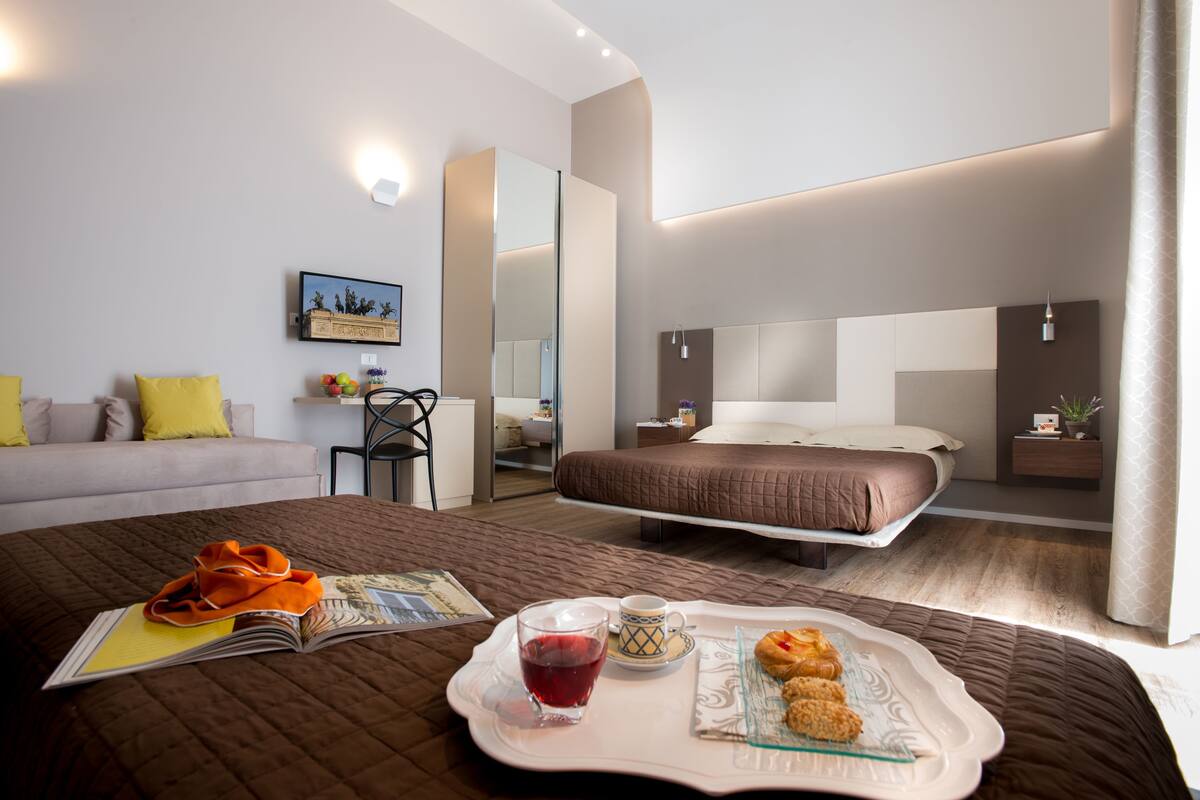 Habitación de hotel moderna con una cama grande, un sofá y una zona de comedor con una bandeja de comida y bebidas.