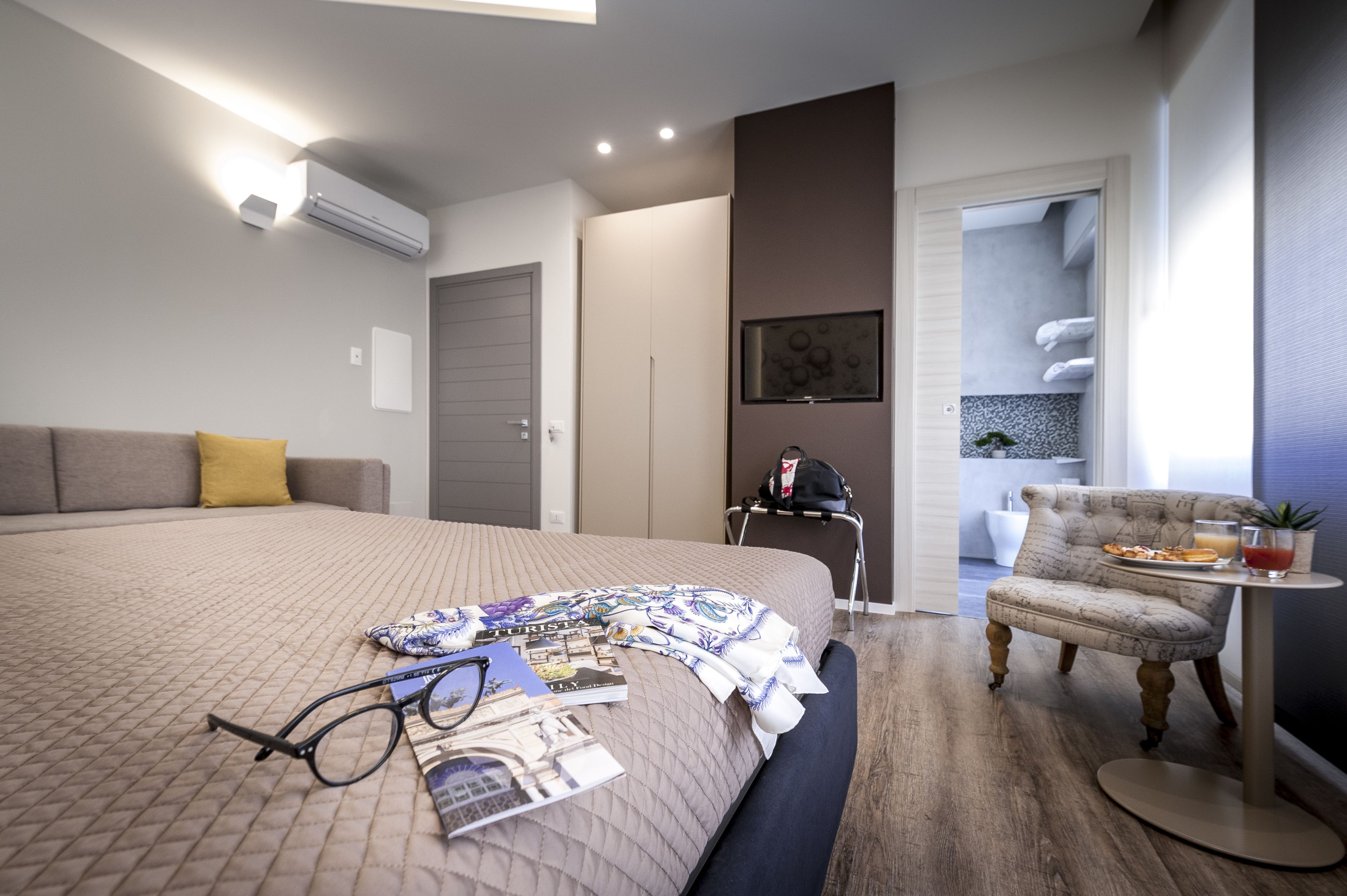 A modern hotel room with a large bed, a seating area with a table, and a view of a bathroom with towels.