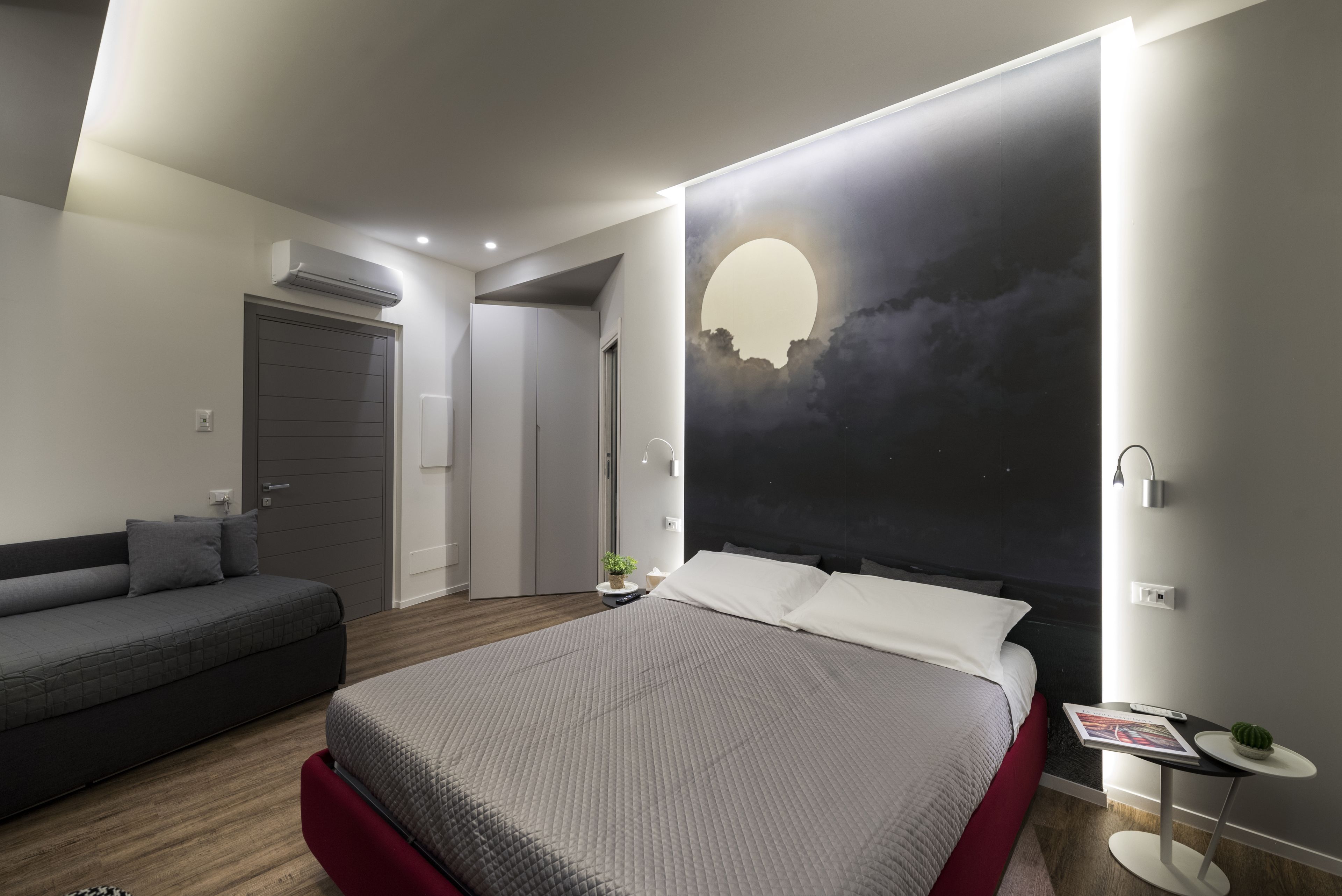 A modern bedroom with a large bed, a sofa, and a wall-mounted artwork.