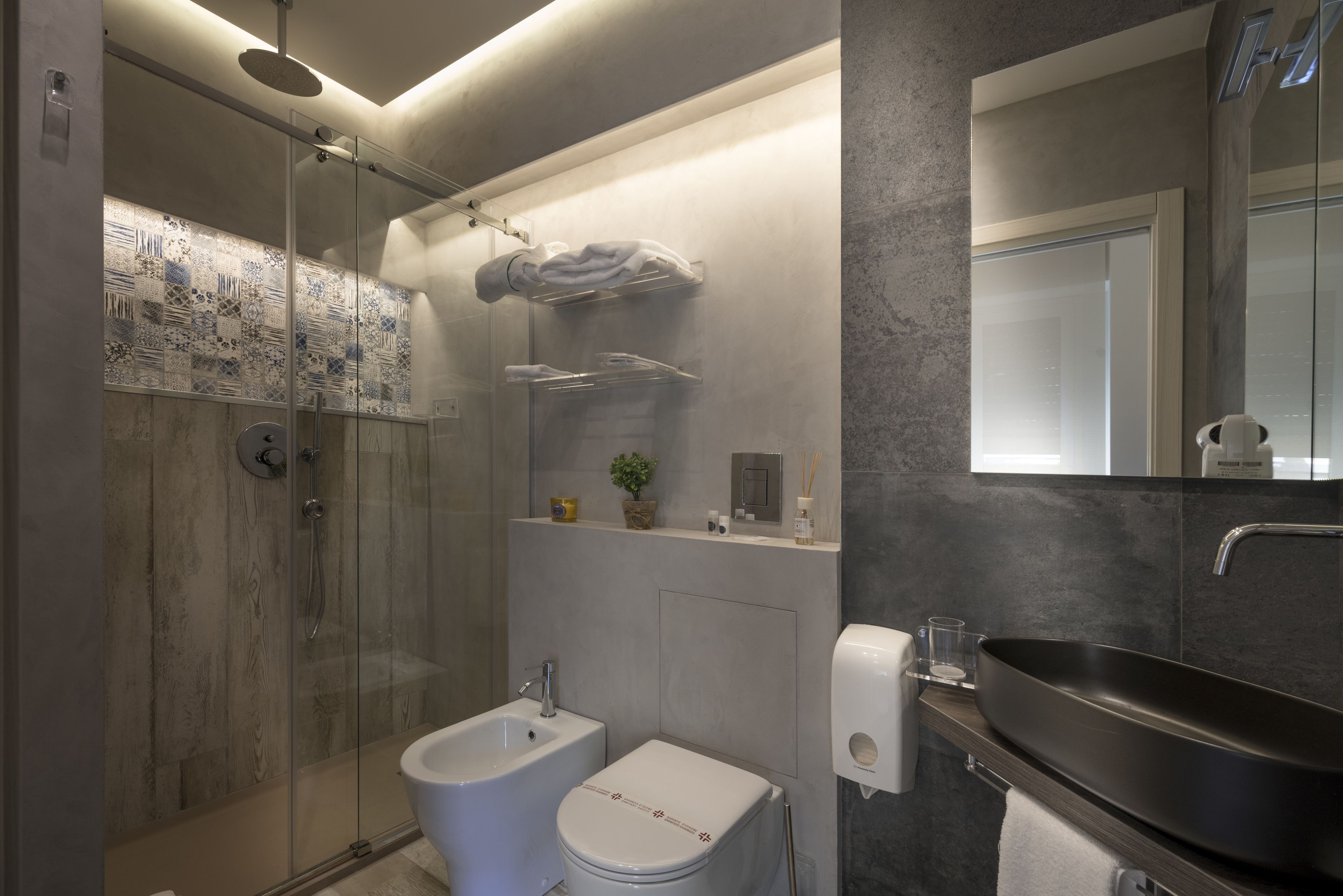 Un baño moderno con ducha acristalada, un bidé, un inodoro, un lavabo grande y un espejo.