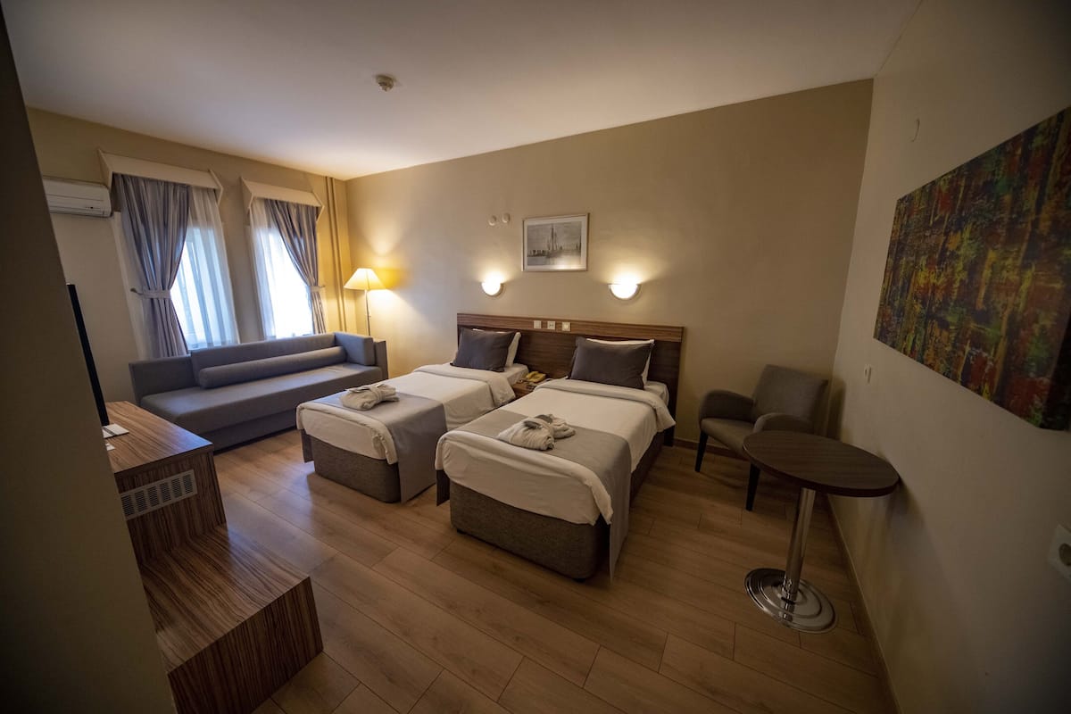 Ein Hotelzimmer mit zwei Betten, einem Schlafsofa, einem kleinen Tisch und einem Stuhl.