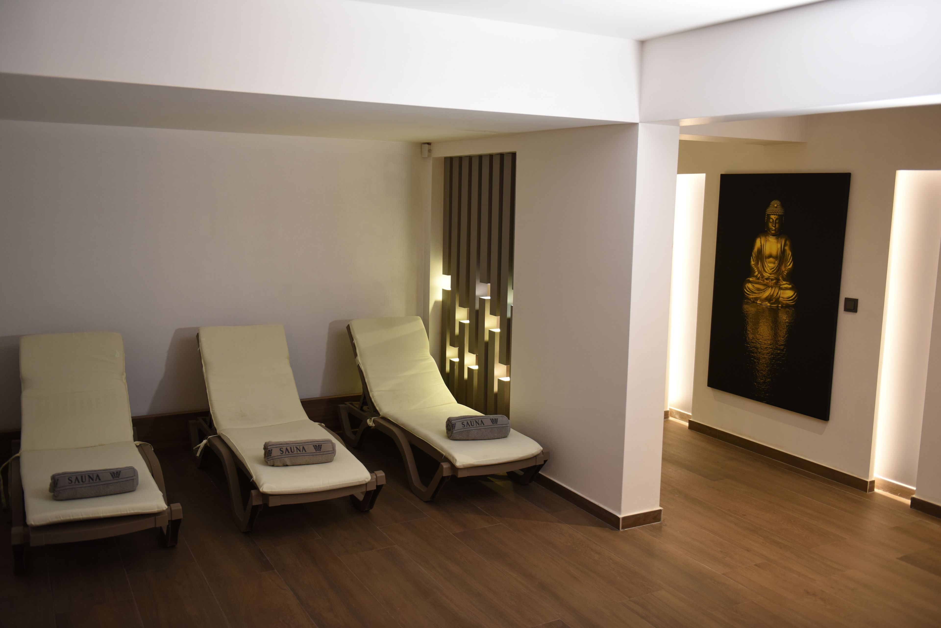 A spa area with three sun loungers, a wooden floor, and a Buddha statue on the wall.