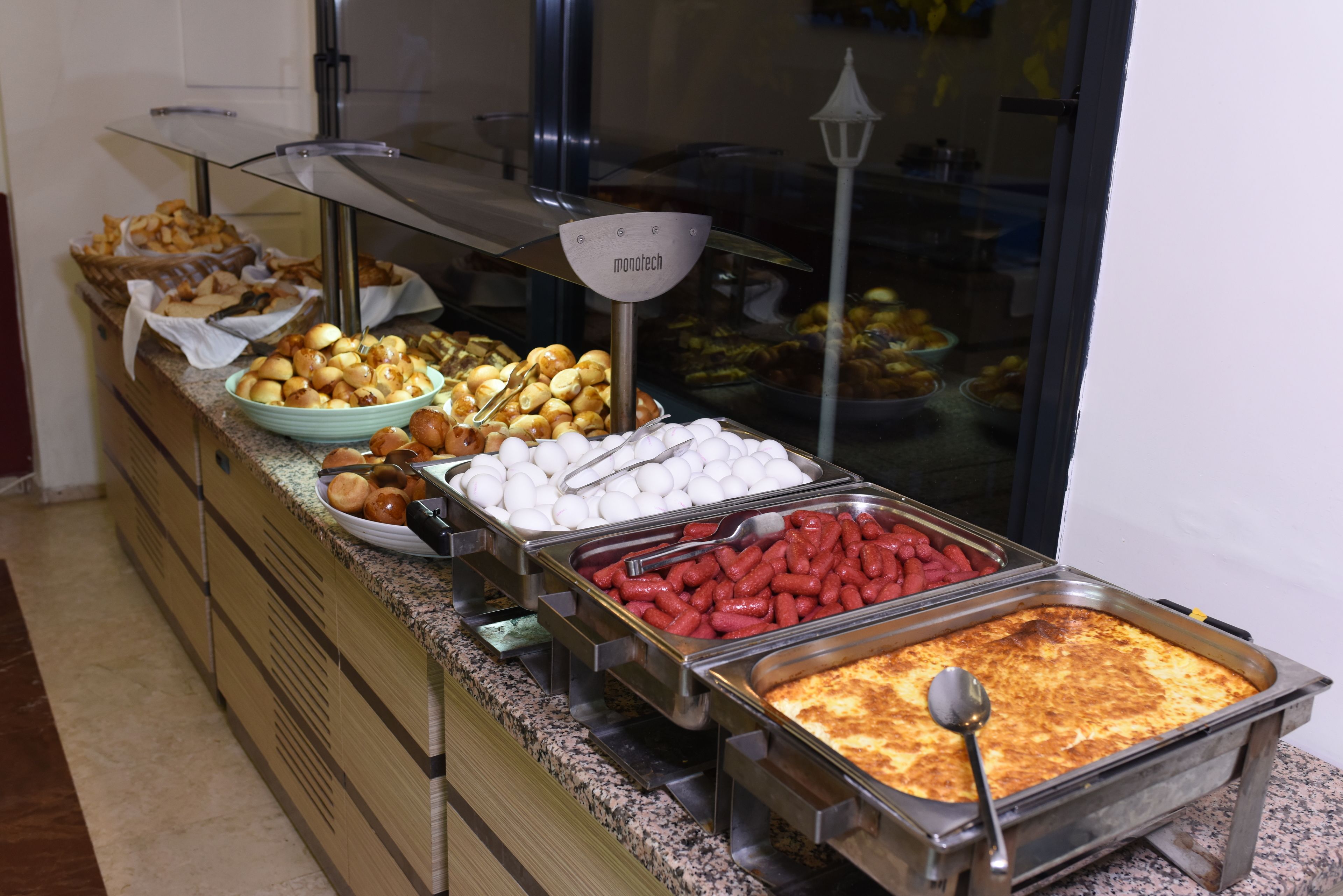A buffet with various food items including pastries, eggs, sausages, and a large serving of lasagna.