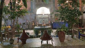 Un interior tradicional marroquí con una fuente central, paredes de azulejos y plantas en macetas.