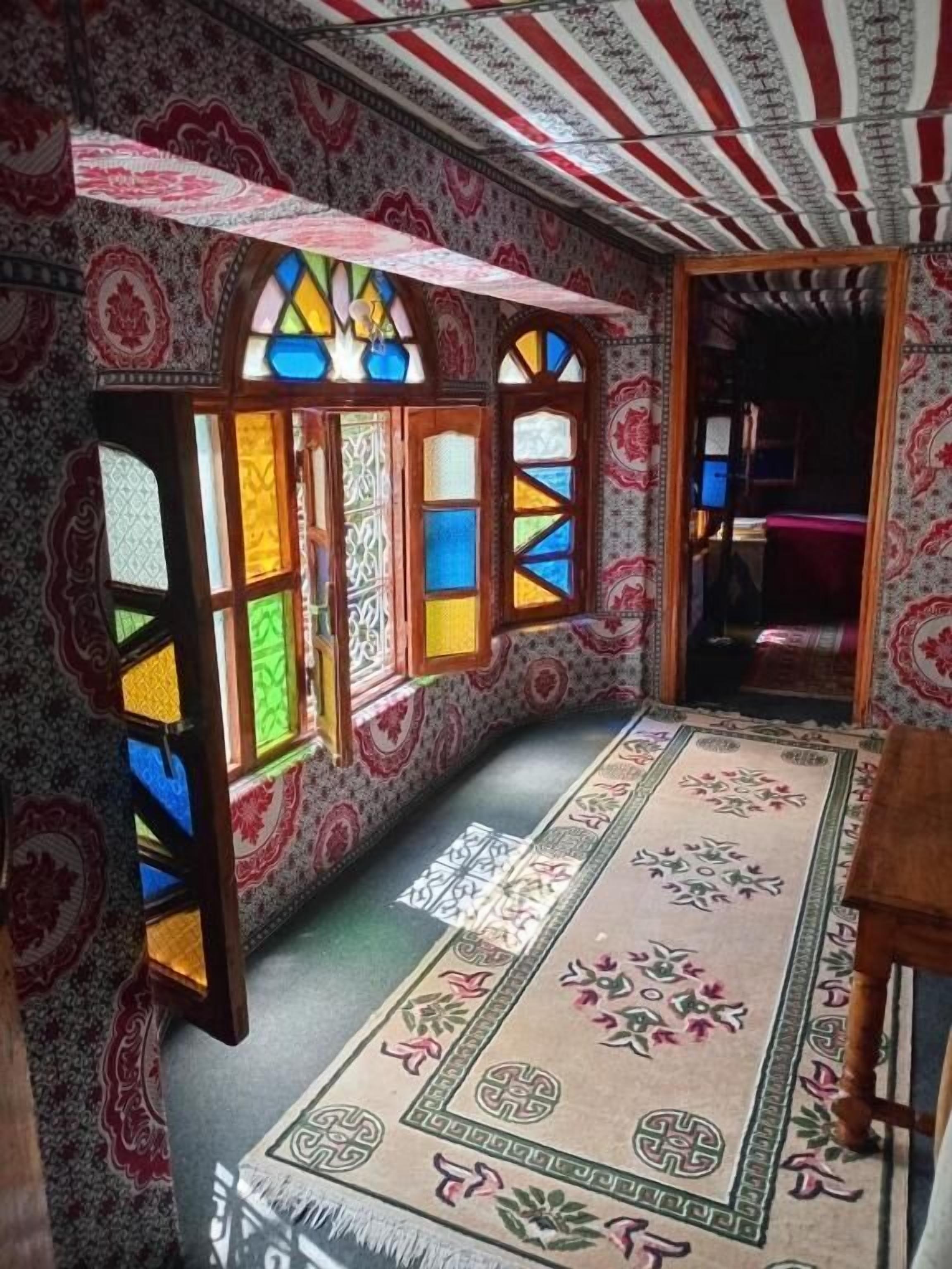 Une pièce aux murs ornés de motifs, un tapis central décoré de motifs floraux et un banc.