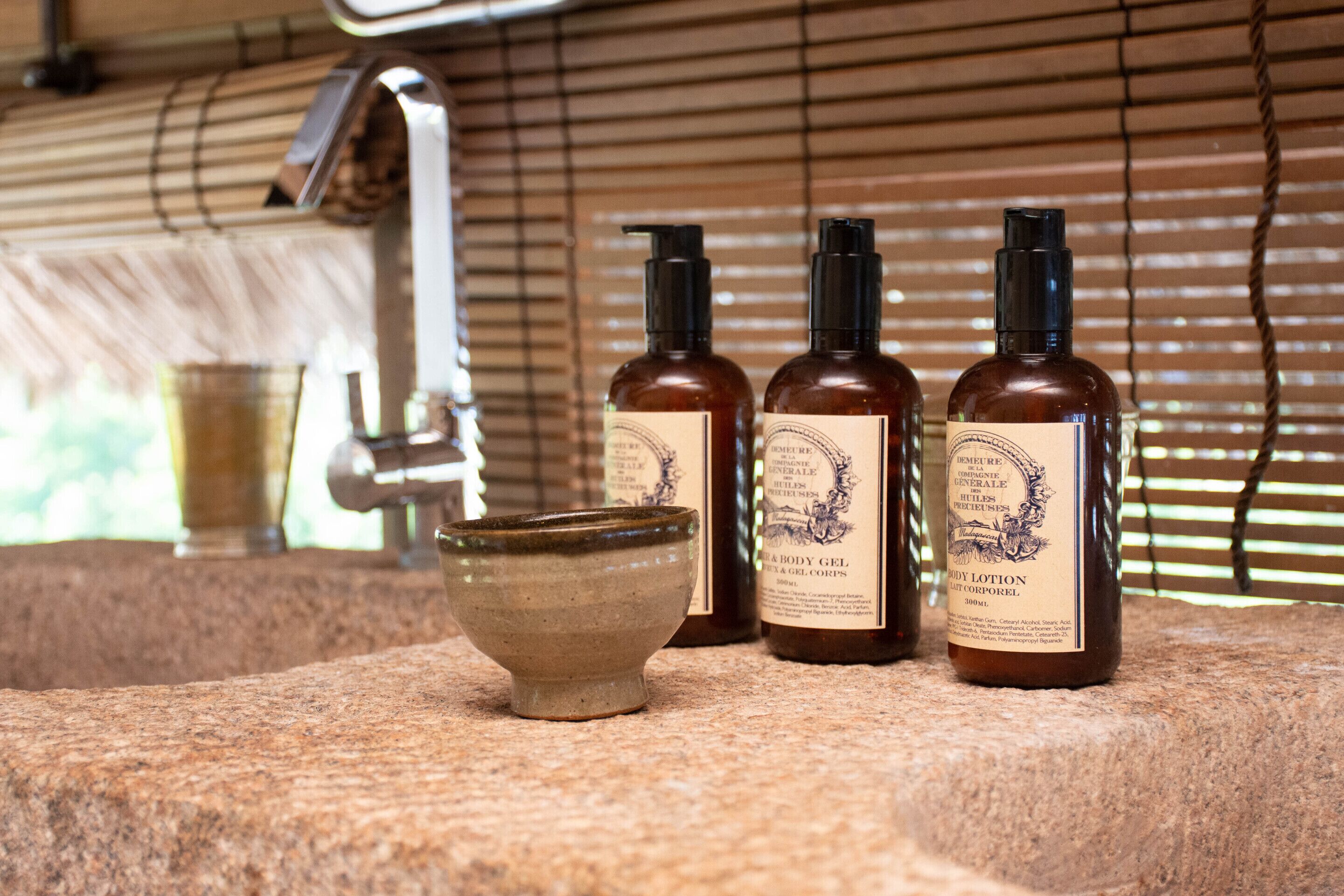 A bathroom with a stone countertop, a ceramic bowl, and three bottles of body lotion.