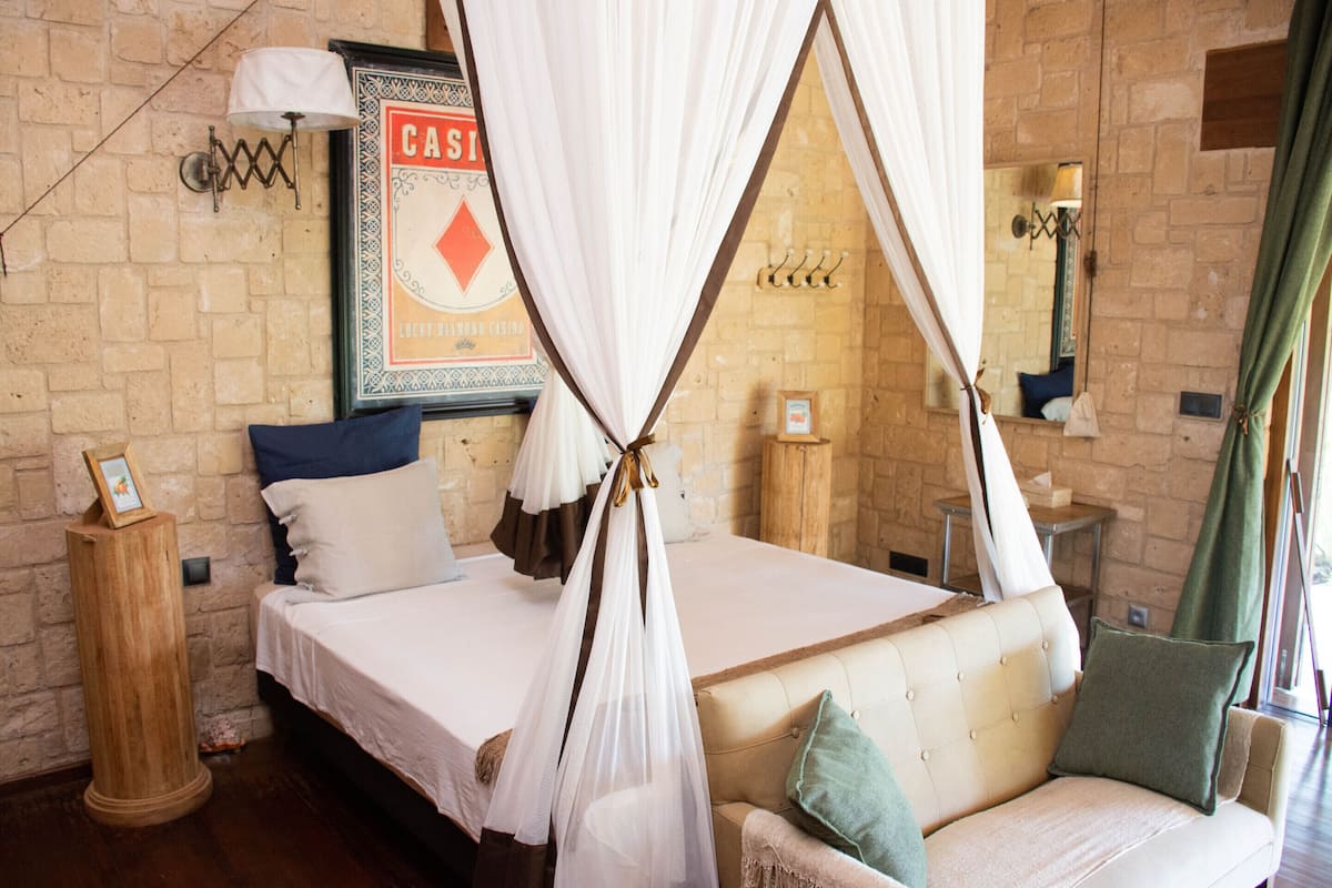 Quarto com cama, sofá, mesa de cabeceira de madeira, luminária na parede e um quadro.