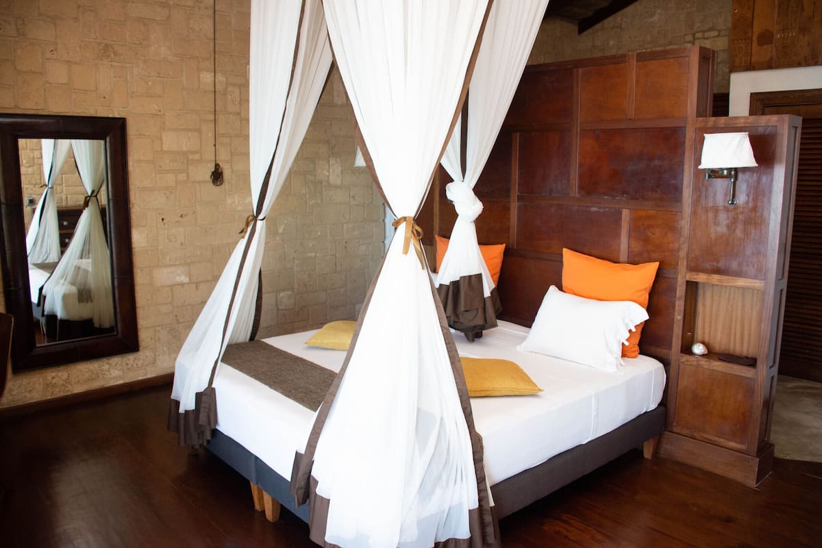 Cama com dossel, cabeceira de madeira e duas almofadas.
