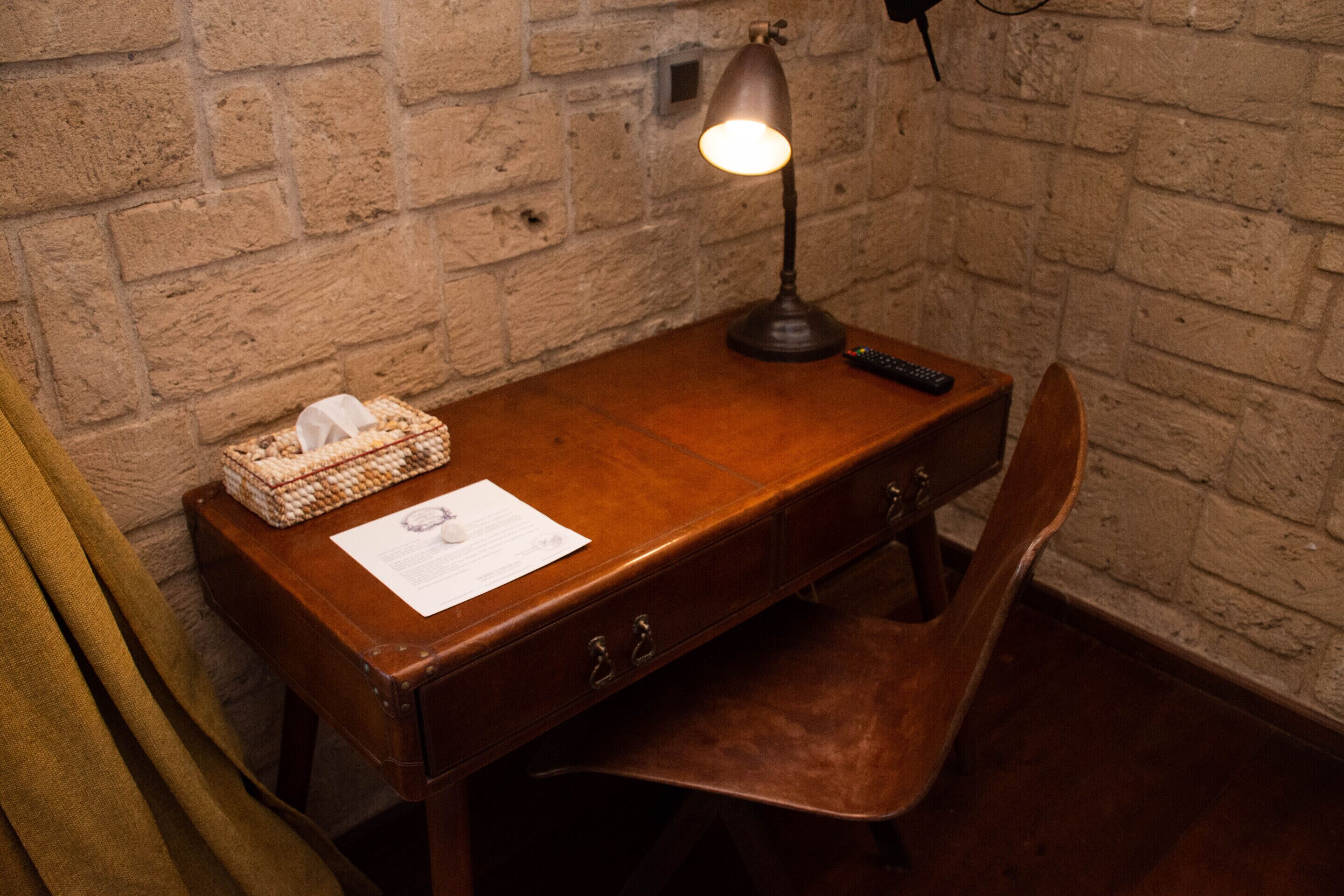 A wooden desk with a lamp, a remote control, a tissue box, and a document on it.