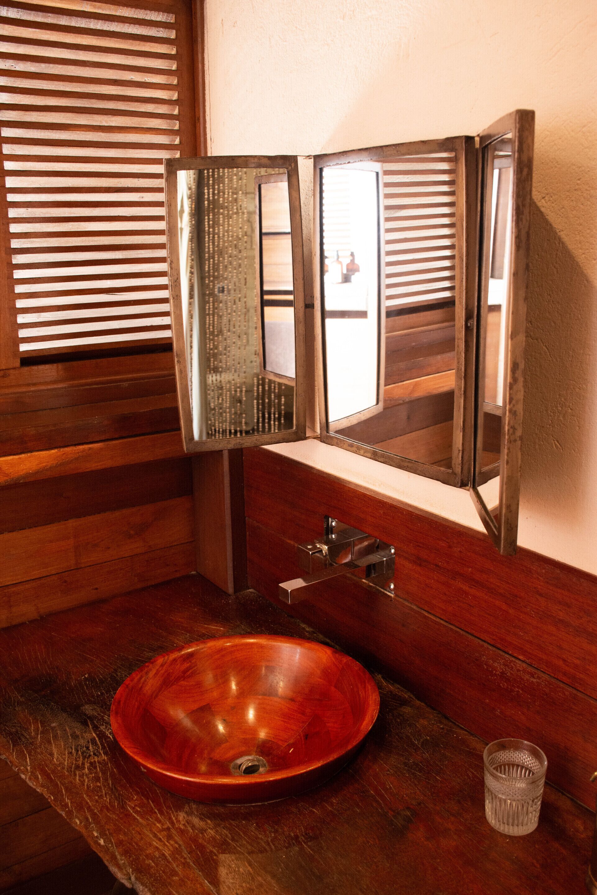 A wooden vanity with a round wooden sink, a mirror, and a glass container.