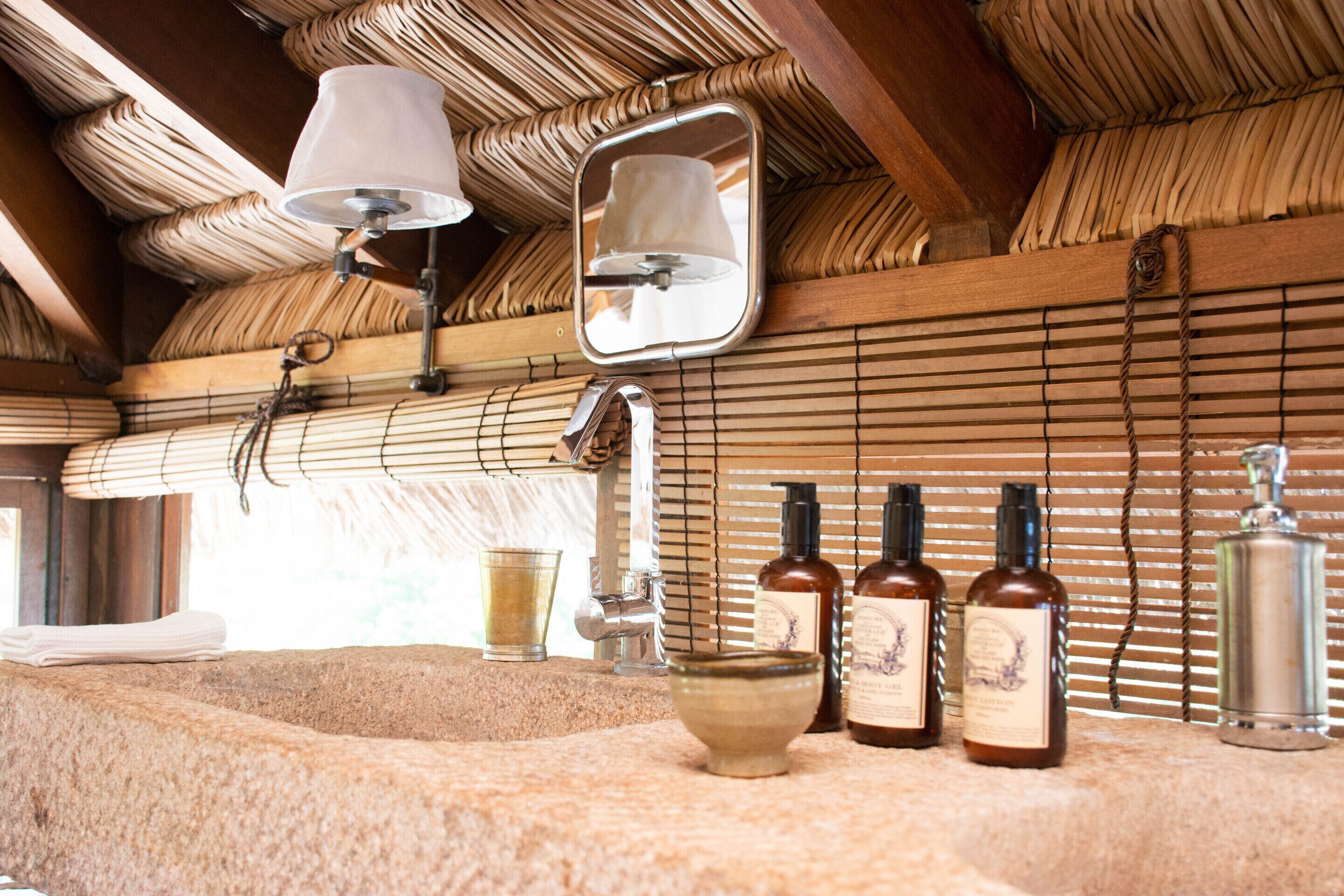 A bathroom with a stone sink, a mirror, and three bottles of liquid.