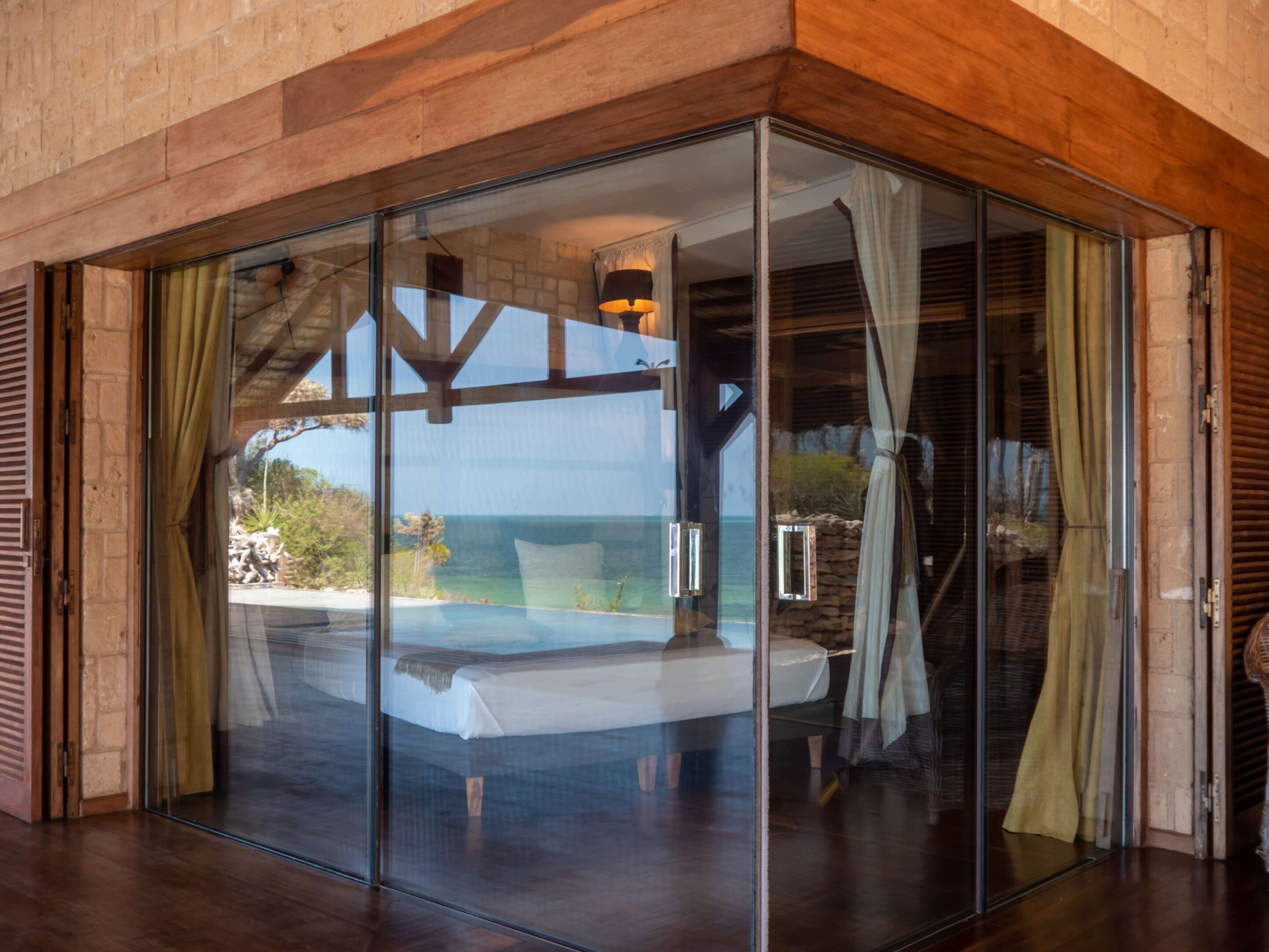 A bedroom with a glass wall, wooden ceiling, and a view of the ocean.
