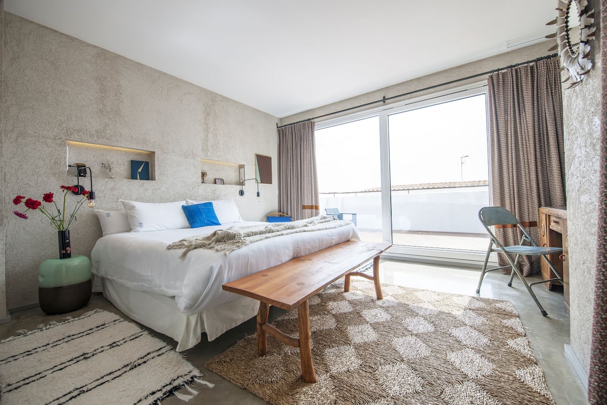 Un dormitorio con una cama grande, un banco de madera, una mesita y una silla.
