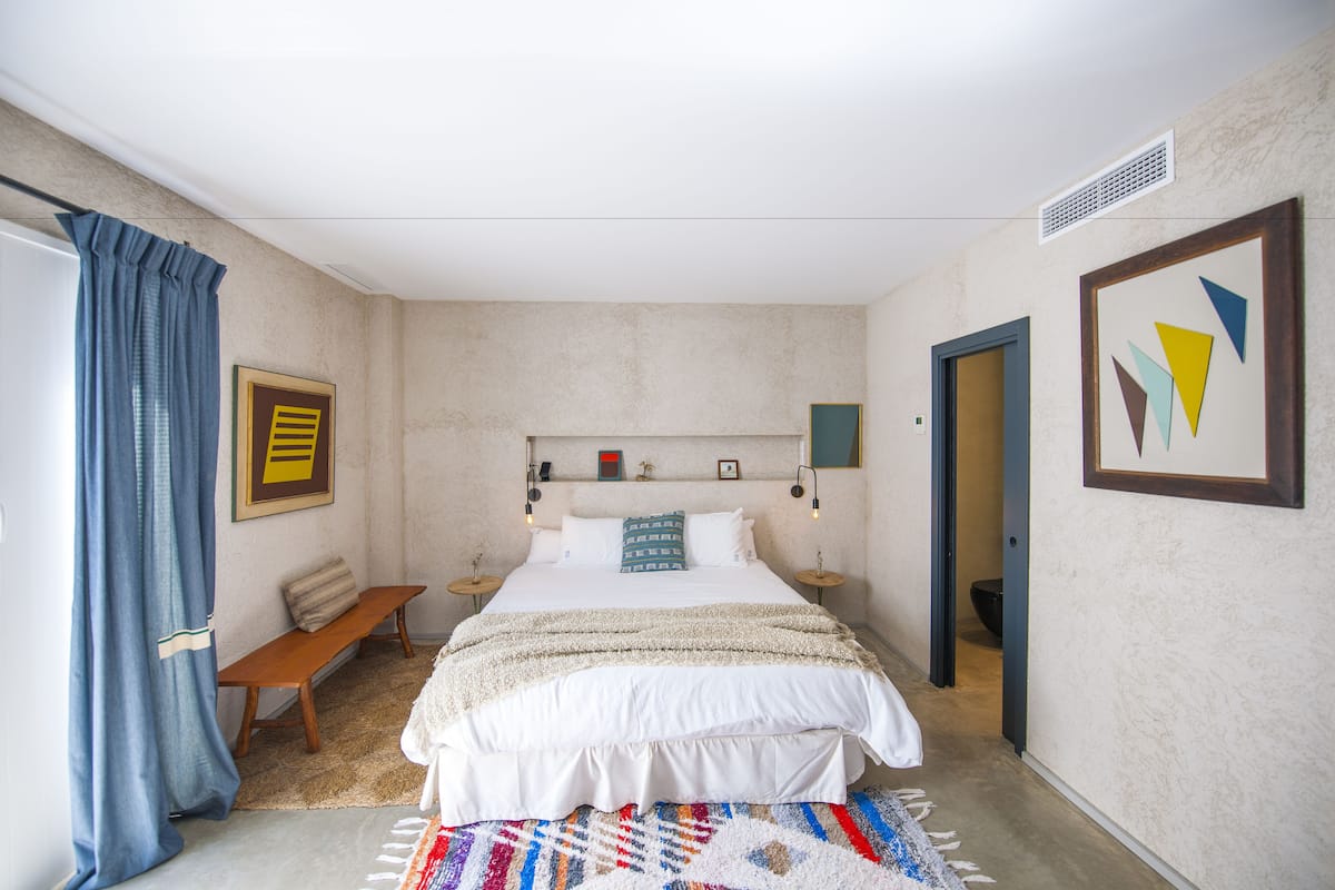 Un dormitorio con cama, un banco, una alfombra y obras de arte en las paredes.