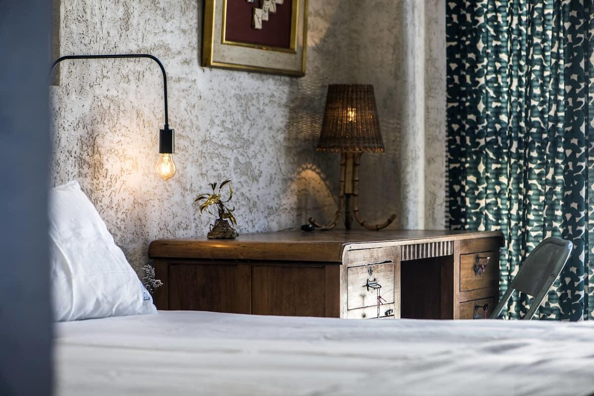 Un dormitorio con un aparador de madera, una lámpara y una cama con ropa de cama blanca.