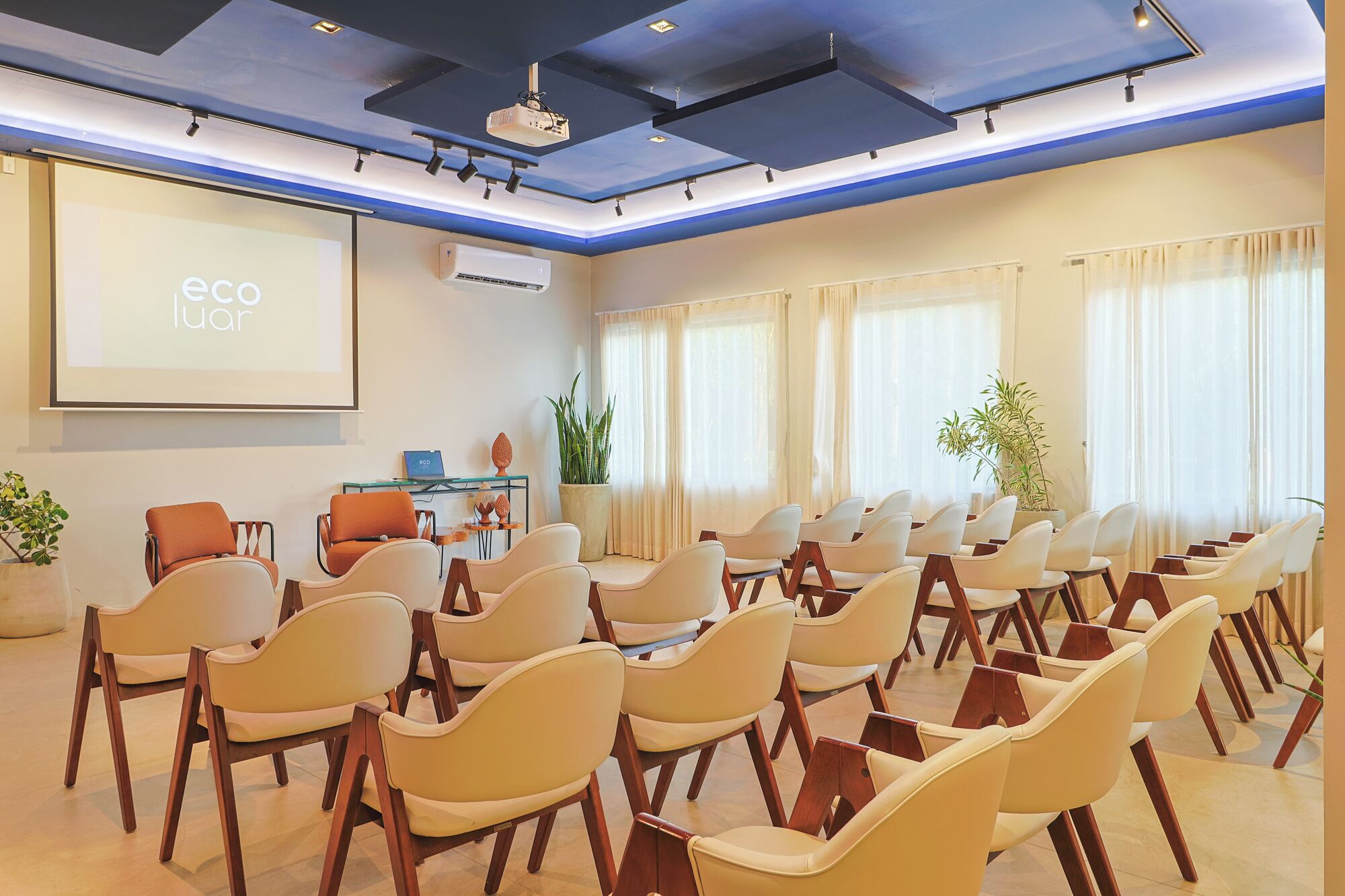 A conference room with rows of chairs, a projector screen, and a small table with a laptop.