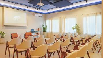 A conference room with rows of chairs, a projector screen, and a small table with a laptop.