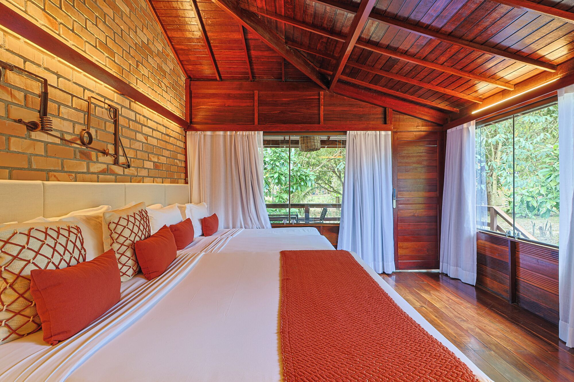 Ein geräumiges Schlafzimmer mit einem großen Bett, Holzboden, Backsteinwand und Blick ins Grüne.