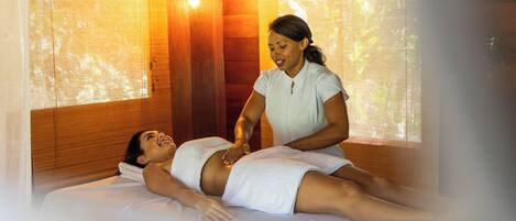 A person receiving a massage in a room with wooden walls and a large window.