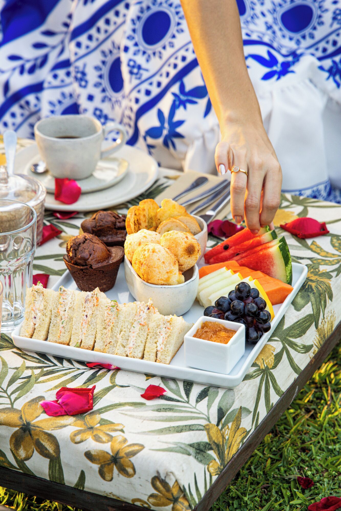 Een tafel gedekt met belegde broodjes, gebak, fruit en een kop koffie.