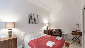 Ein Hotelzimmer mit Bett, Sessel, Schreibtisch, Lampe und einem Wandbild.
