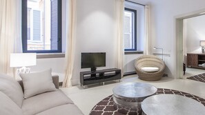 Ein modernes Wohnzimmer mit einer Couch, einem Fernseher, einem Korbsessel und einem runden Couchtisch.