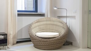 Une chaise en osier avec un coussin, dans une pièce dotée d’une fenêtre, d’un lampadaire et d’un radiateur.
