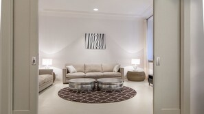 Ein modernes Wohnzimmer mit einem beigefarbenen Sofa, zwei Beistelltischen, einem runden Couchtisch und einem gemusterten Teppich.