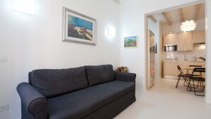 Ein modernes Wohnzimmer mit grauem Sofa, einem Essbereich mit Tisch und Stühlen und einer durchgehenden Tür erkennbaren Küche.