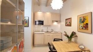 Una cocina compacta con electrodomésticos modernos, un comedor con mesa de madera y obras de arte en las paredes.