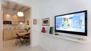 Eine moderne Küche mit Holzschränken, einem Esstisch und Stühlen. Ein Flachbildfernseher ist an der Wand über einem Regal mit Dekorationen angebracht.