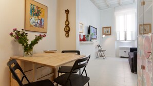 Ein Essbereich mit einem Holztisch und Stühlen, einer Vase mit Blumen, einer Uhr und einem Gemälde an der Wand.