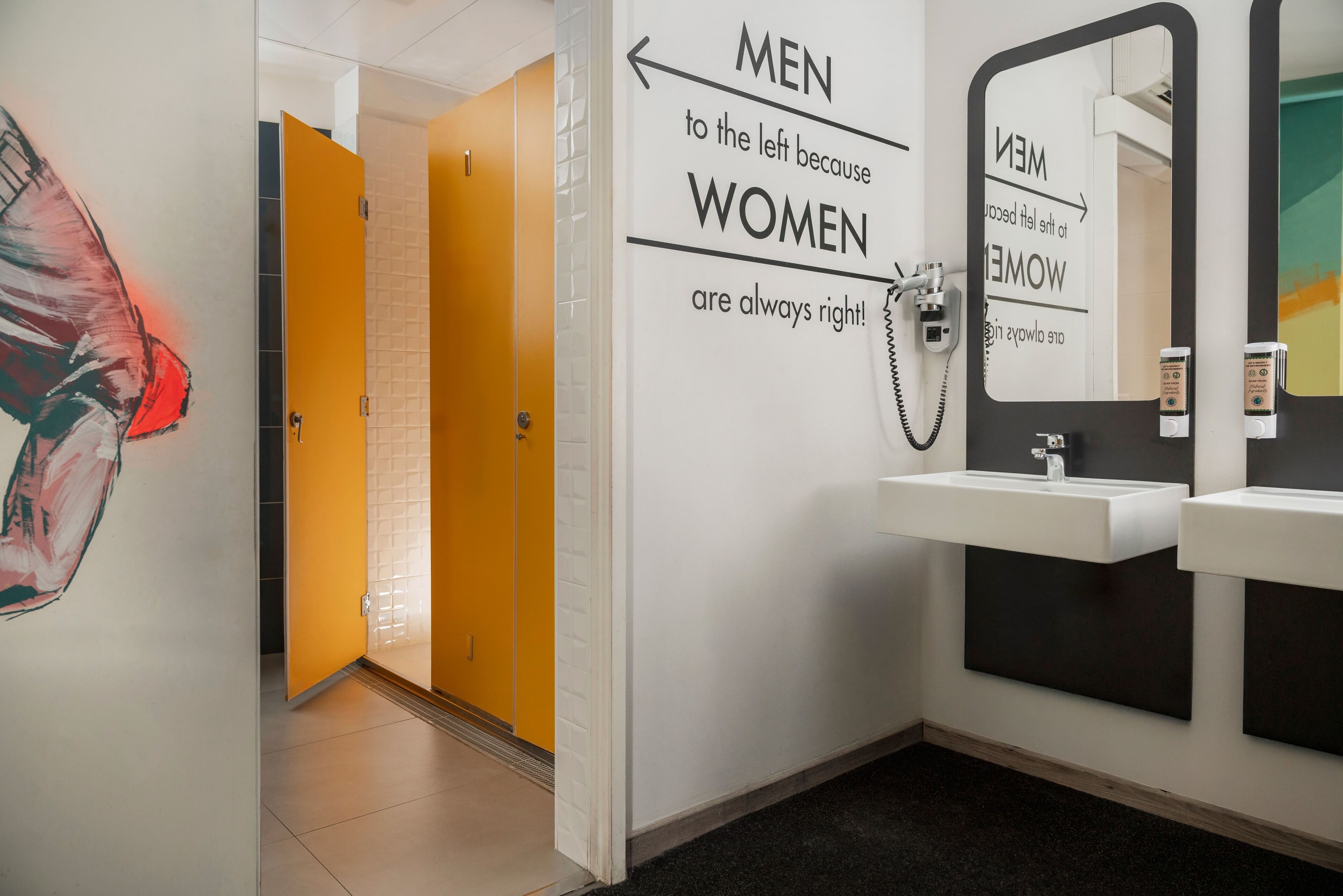 Une salle de bain équipée d’un miroir, d’un lavabo et d’un panneau mural indiquant les toilettes réservées aux hommes ou aux femmes.