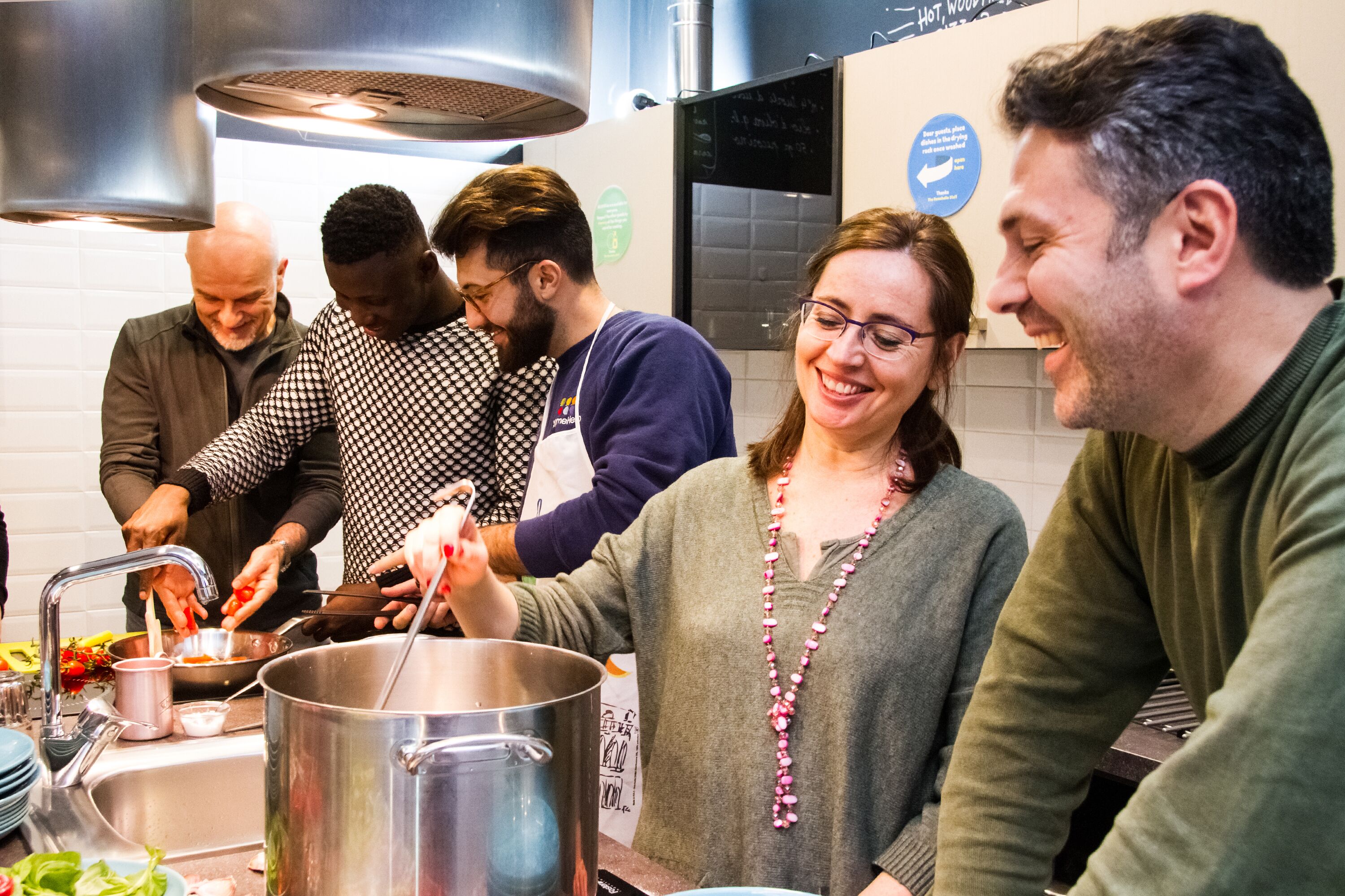 A group of people preparing food in a kitchen with stainless steel appliances and a large pot.