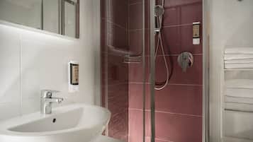 Un baño con lavamanos blanco, ducha con mampara de vidrio y un perchero para toallas.