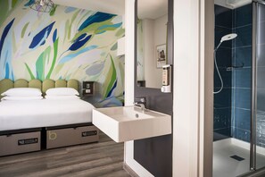 A modern hotel room with a bed, a wall-mounted sink, and a shower.