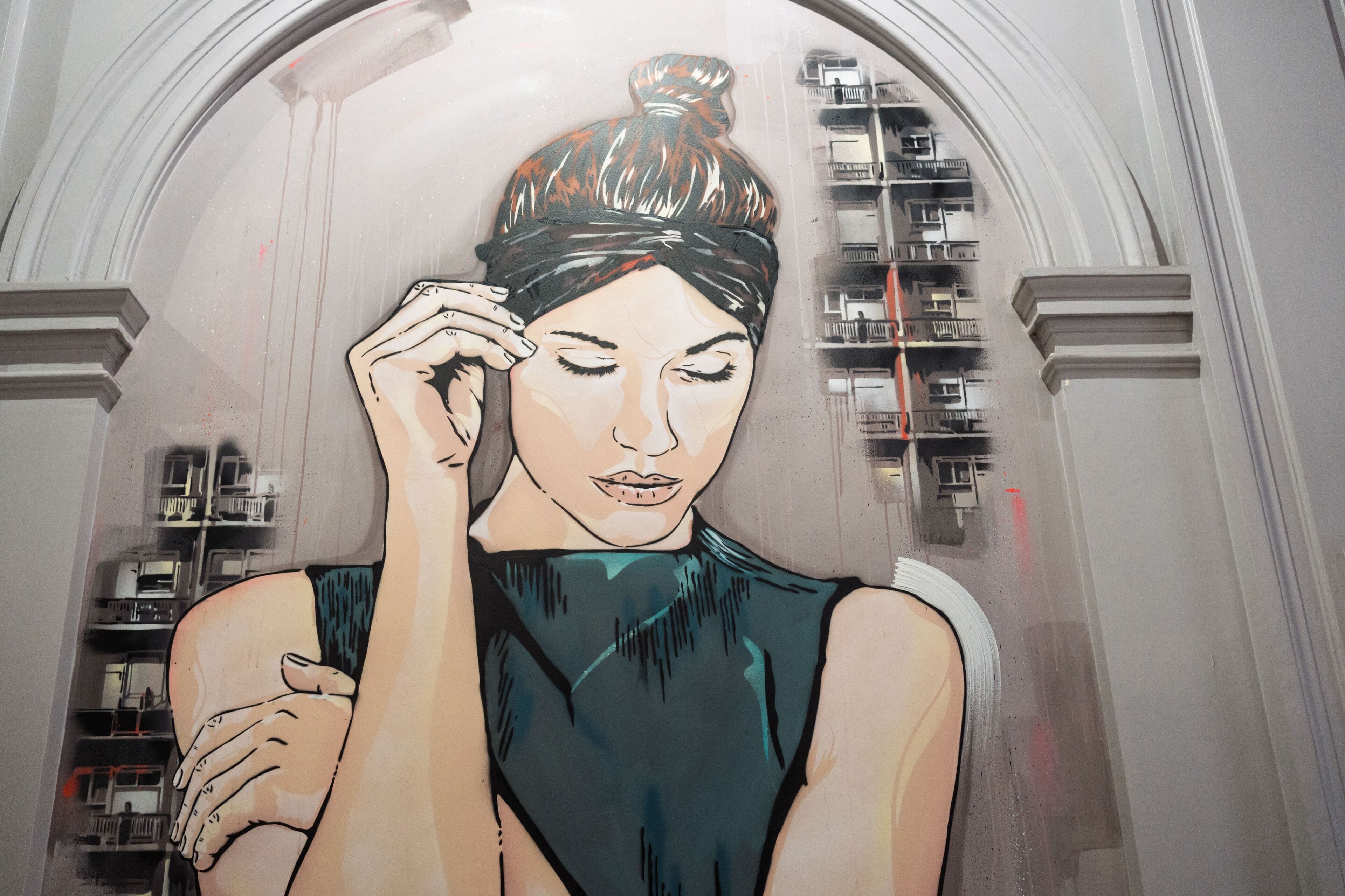 A mural of a woman in a sleeveless top with a bun hairstyle, set against a building facade with balconies.