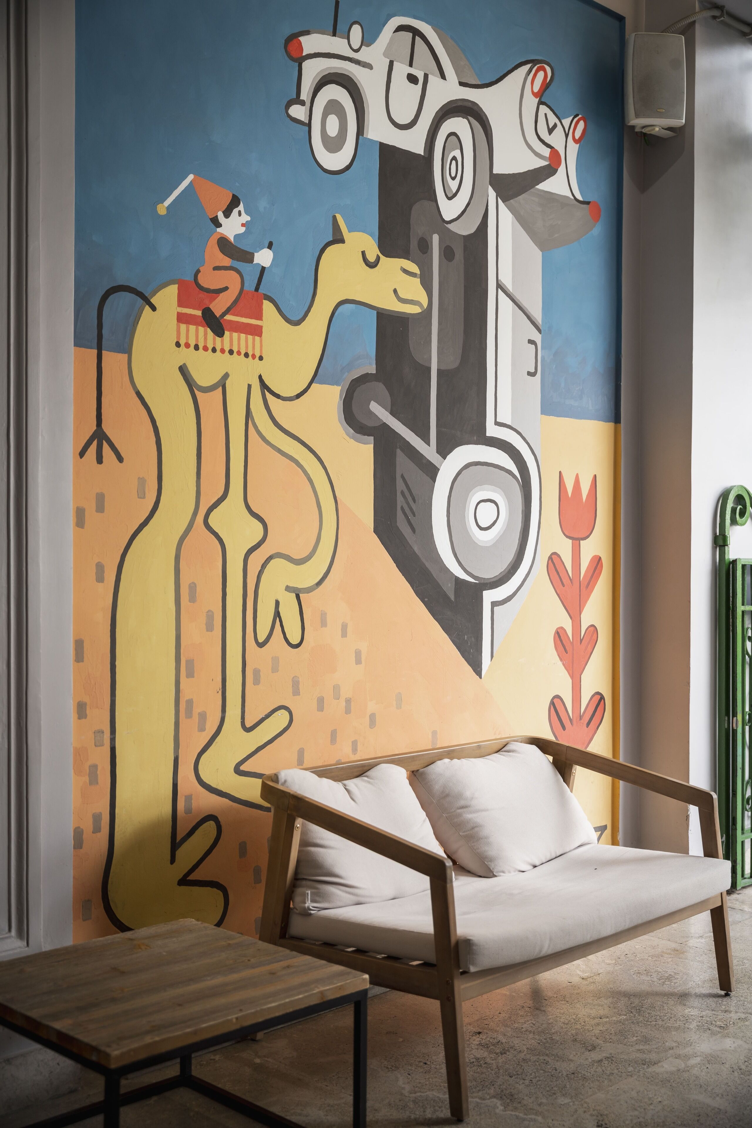 A room with a sofa, a small wooden table, and a colorful mural on the wall.