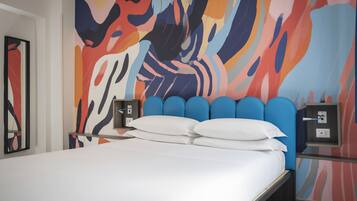 Una habitación de hotel moderna con una cama grande, un mural abstracto colorido y una mesita de noche con una lámpara.