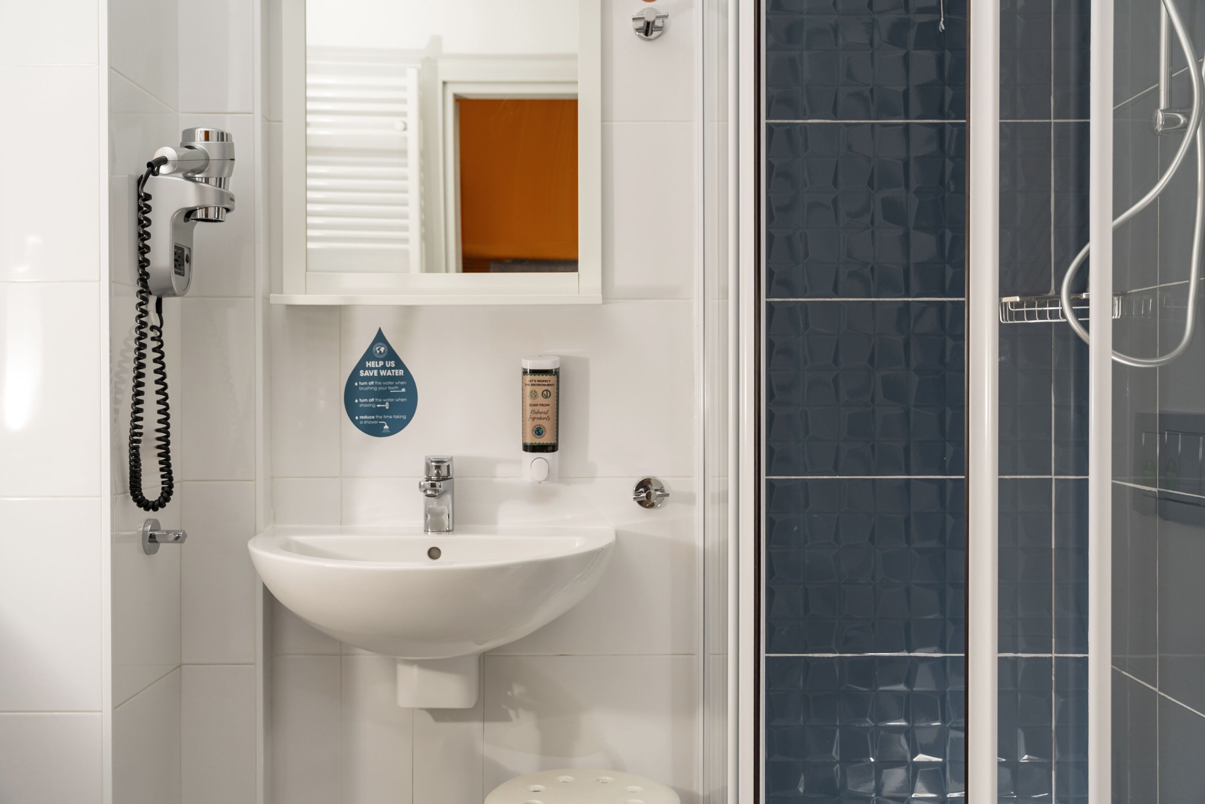 Un baño con un lavabo blanco, un espejo, cabina de ducha y un perchero para toallas.