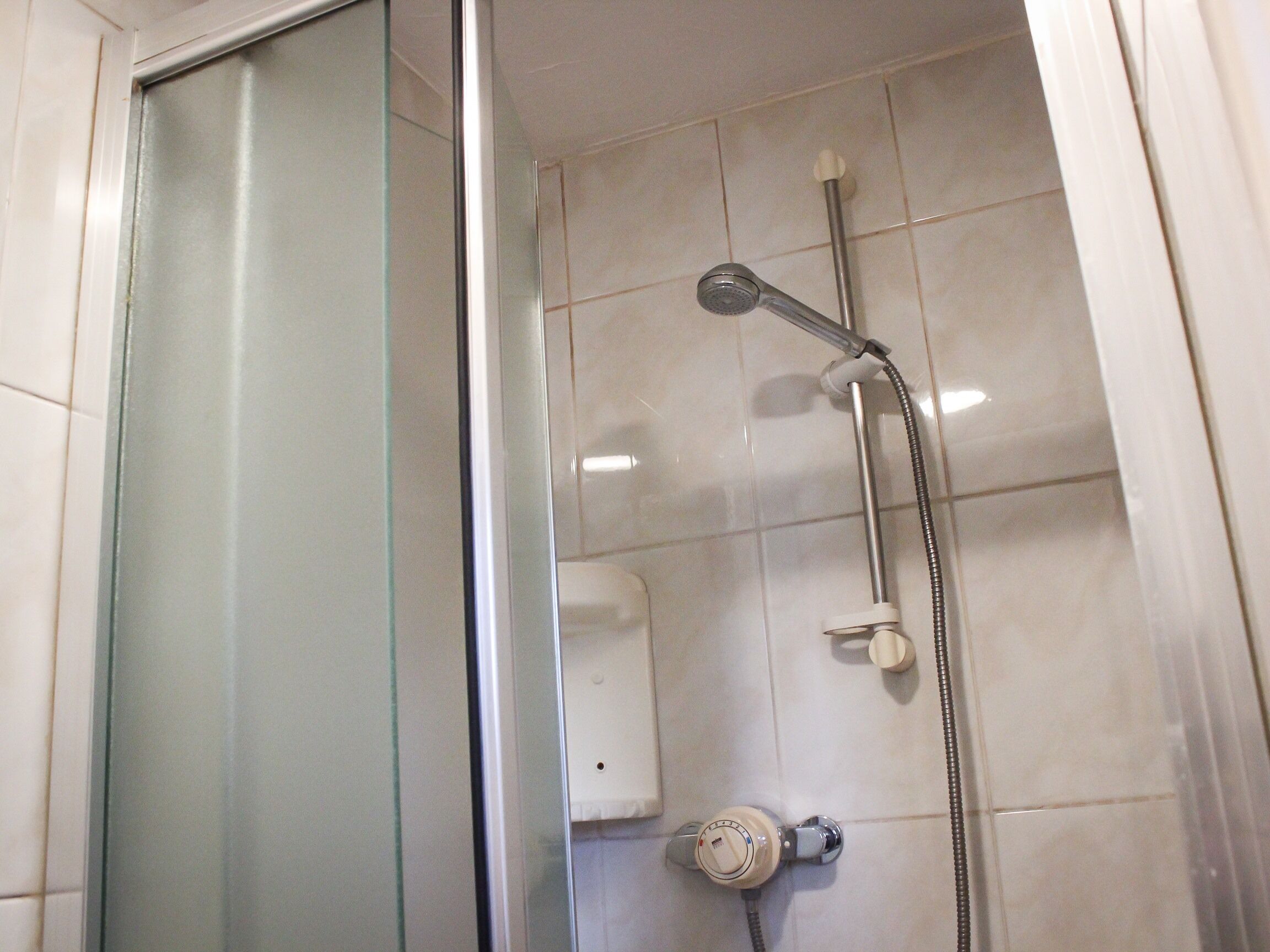 A shower with a glass door, a handheld showerhead, and a wall-mounted control panel.