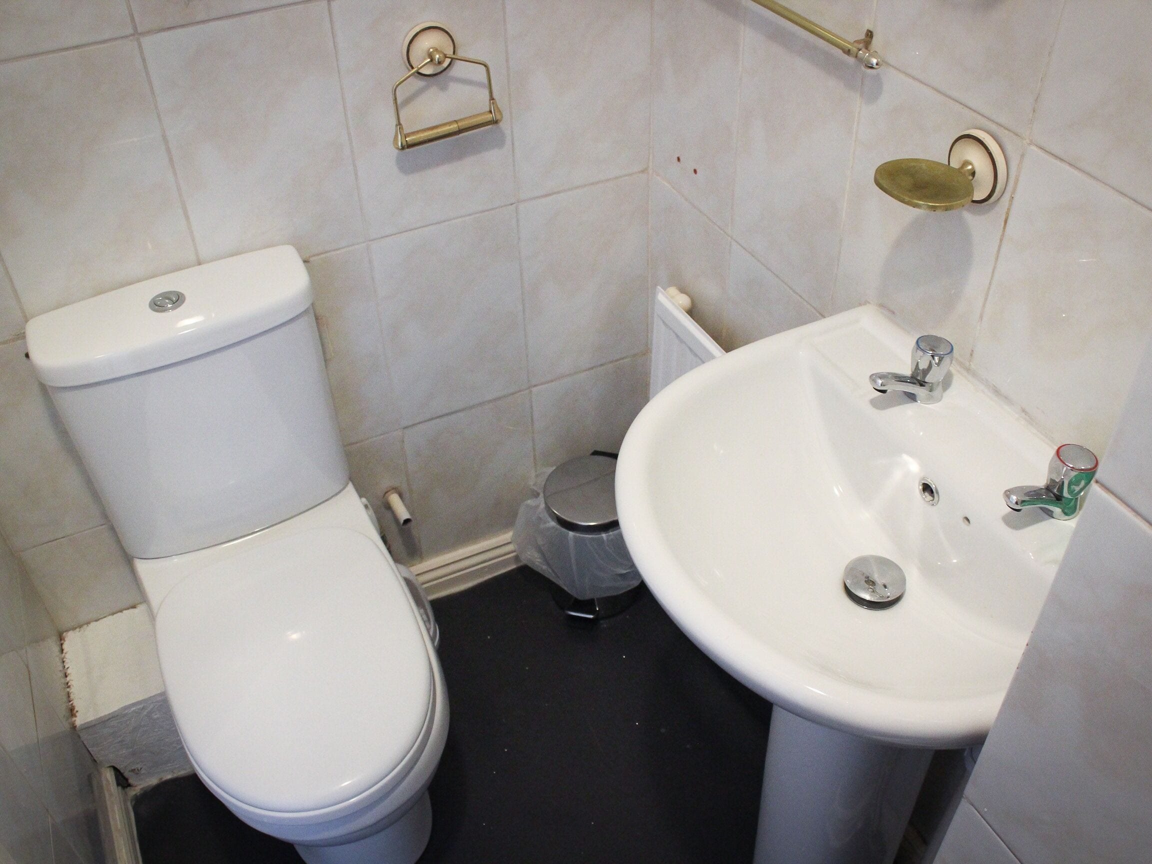 A bathroom with a toilet, sink, and a trash bin.