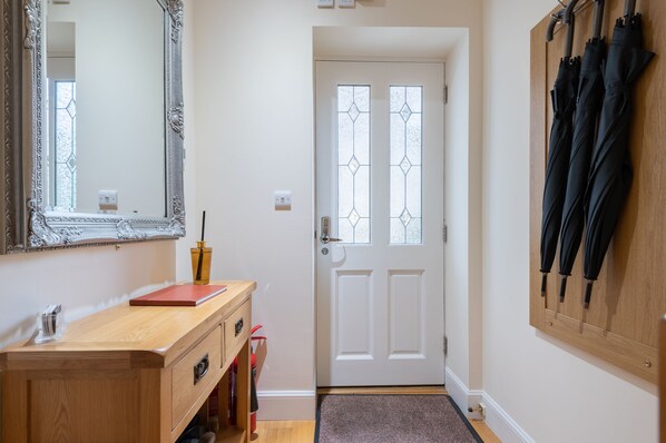 Un pasillo con un tocador de madera, una puerta blanca con paneles de vidrio y un perchero de paraguas en la pared.