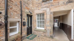A narrow stone corridor with a black door, a small window with blinds, and a welcome mat. - 138 North Street (St. Andrews)