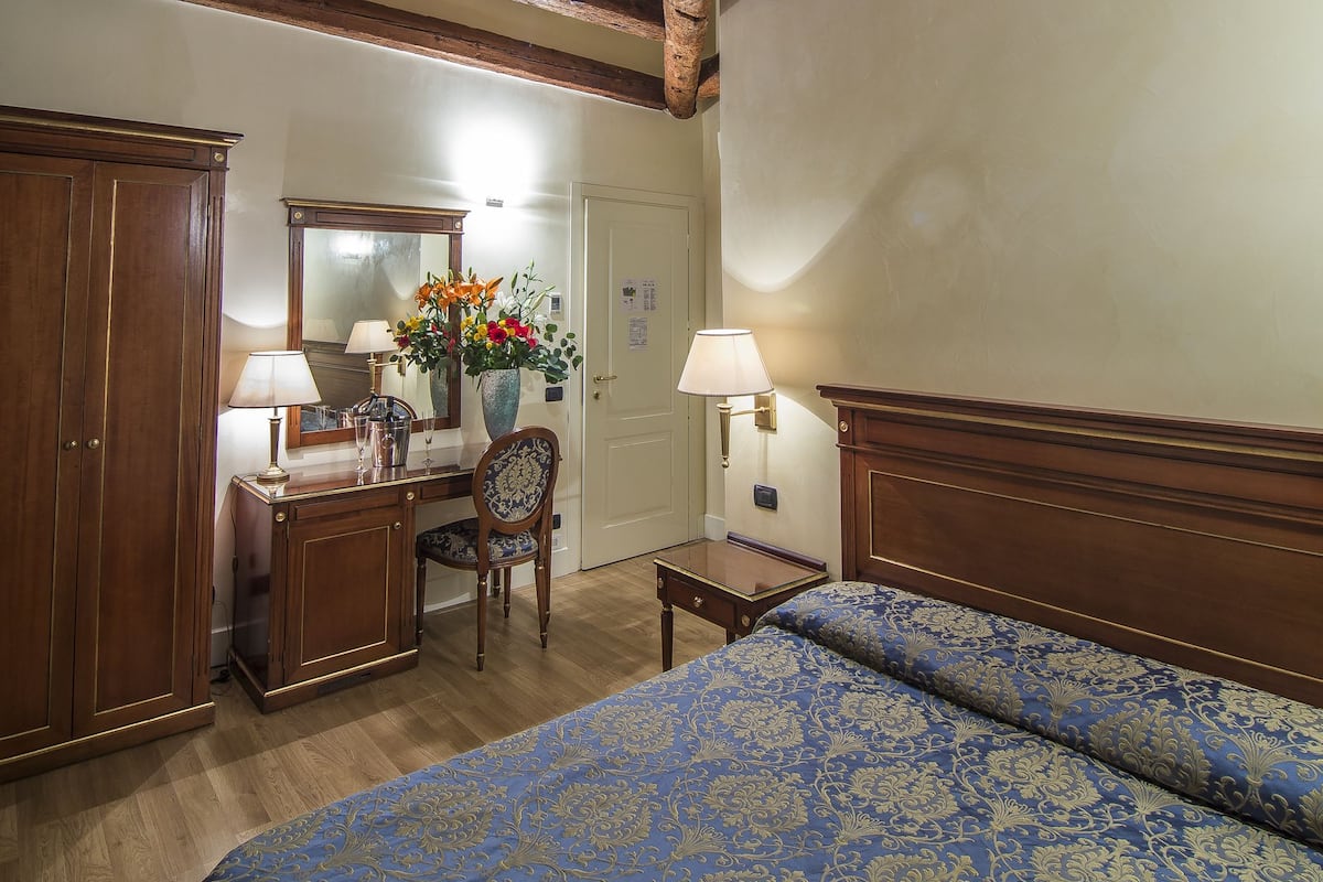 Un dormitorio con techo de madera, una cama con colcha estampada en azul, un escritorio con espejo y una silla.